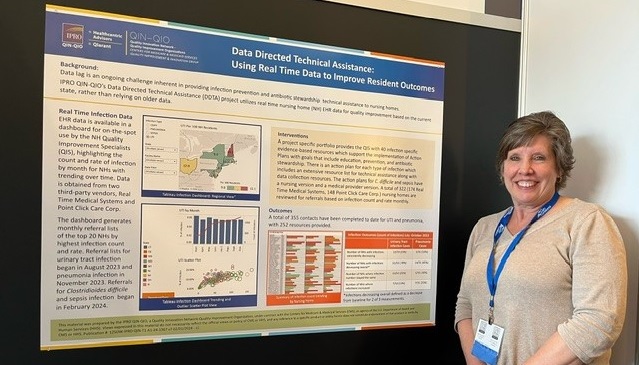 Smiling woman with short hair standing next to a poster on display at a conference.