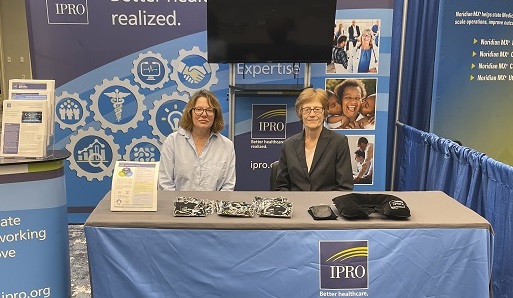 Two white women sitting behind a desk at a conference where IPRO has a display booth