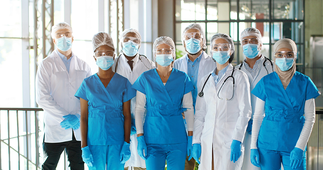 Team of mixed-races team of professional males and females doctors in hospital. Indoor. International group of medics in medical masks. Multi ethnic physicians in gowns and uniforms in clinic.