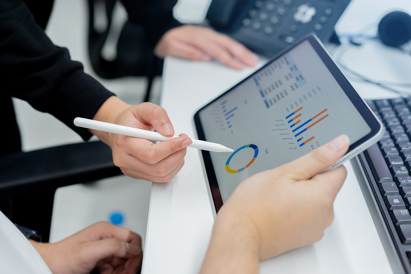 close up of hands holding a tablet while someone points to a graph being displayed on the screen