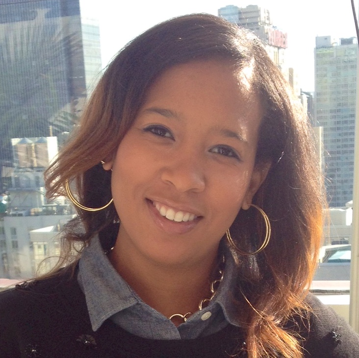 Photo of an African American woman smiling at the camera with tall buildings in the background.