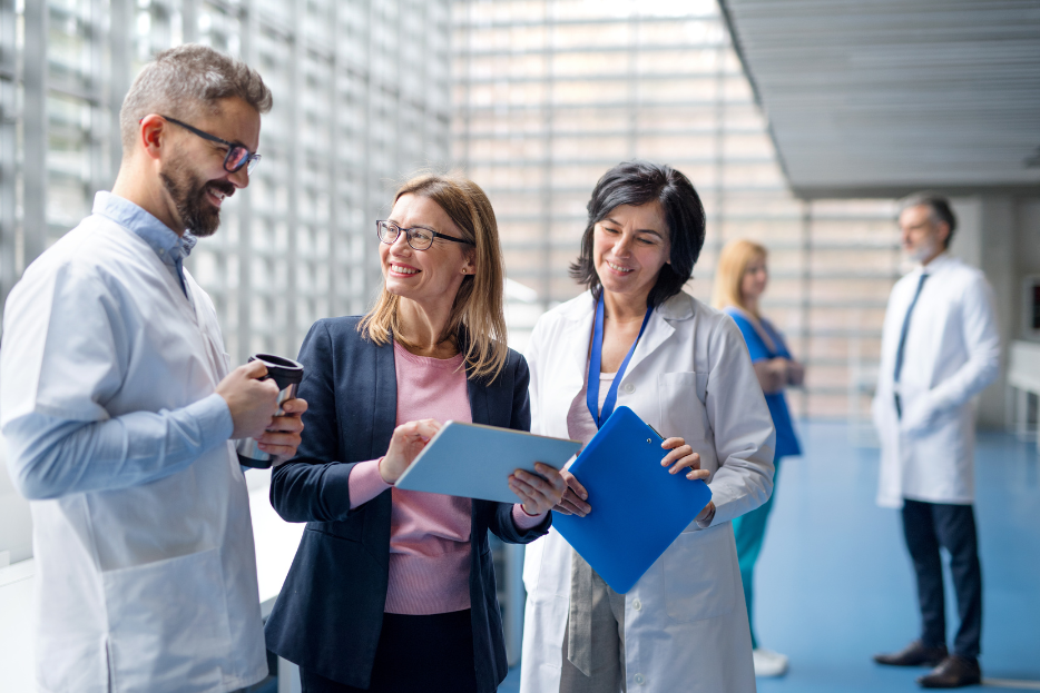 Male clinician and female clinician in white coats are talking to a woman in a business suit in a hallway