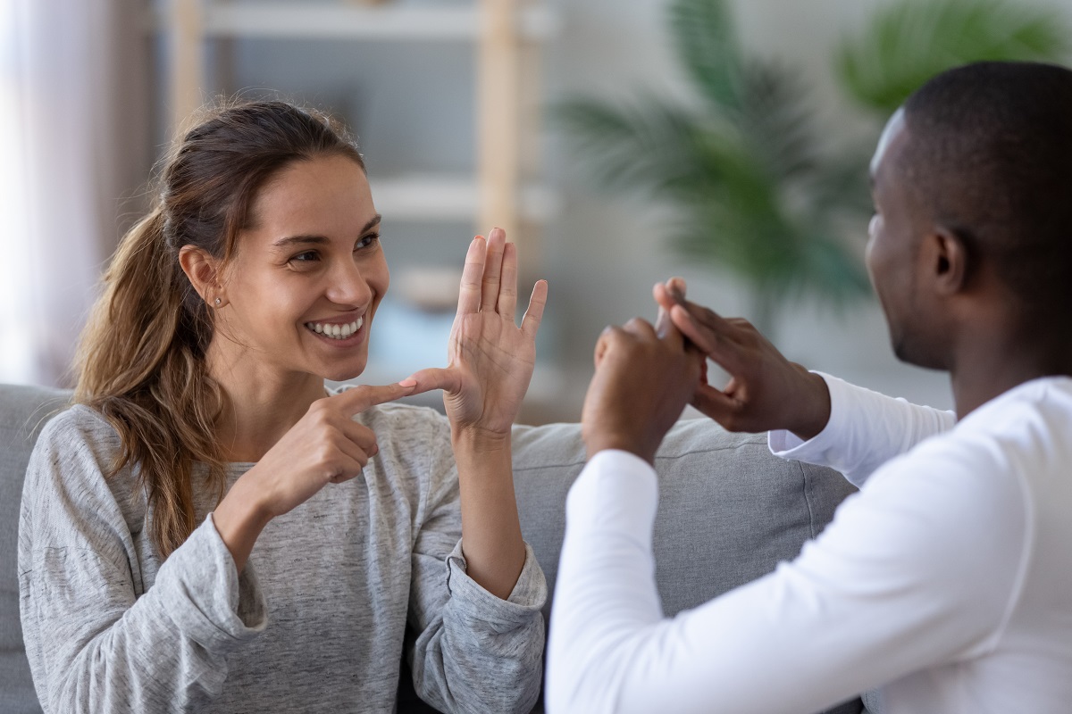 Smiling mixed ethnicity couple or interracial friends talking with sign language